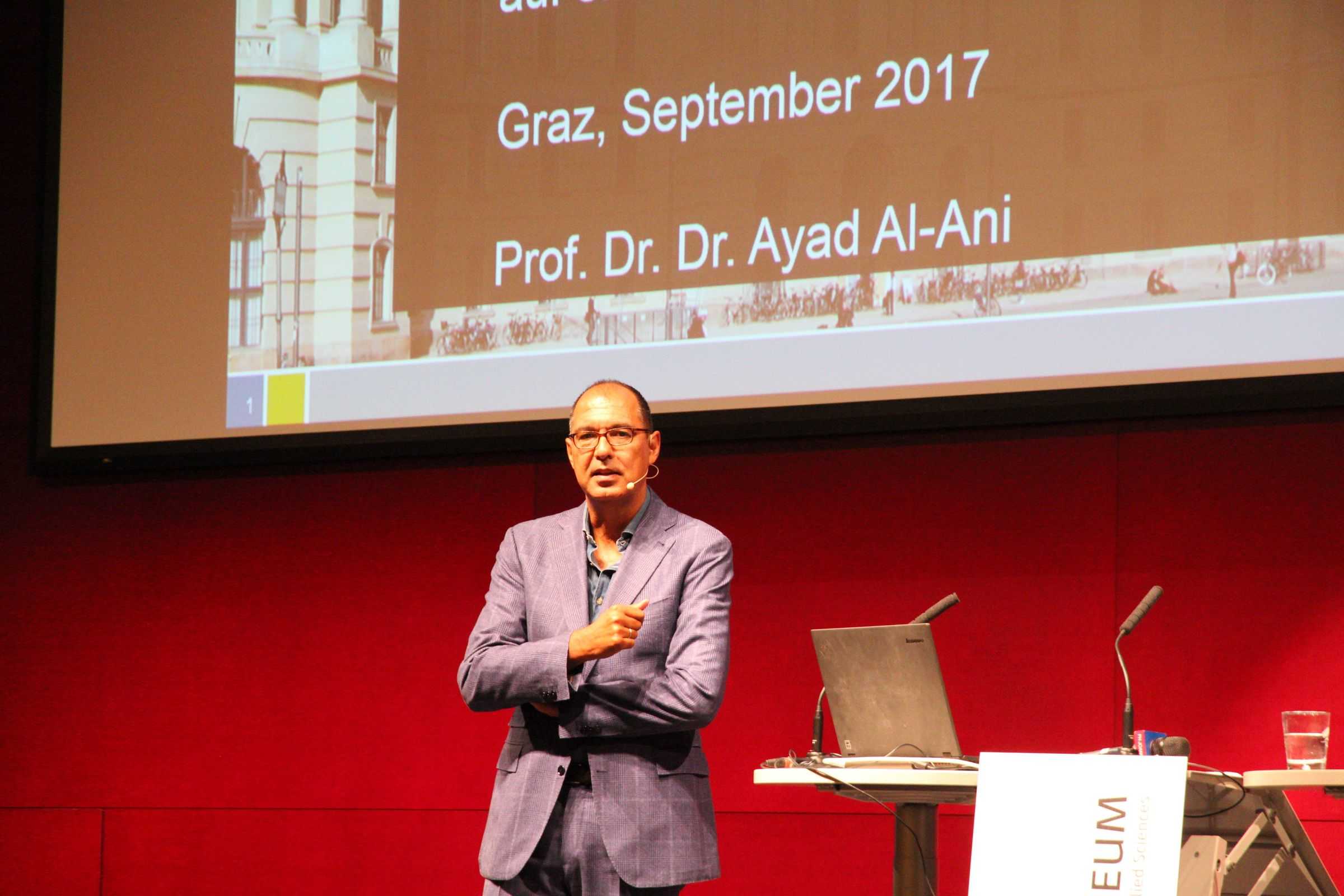 Foto von Ayad Al-Ani mit Präsentation im Hintergrund.