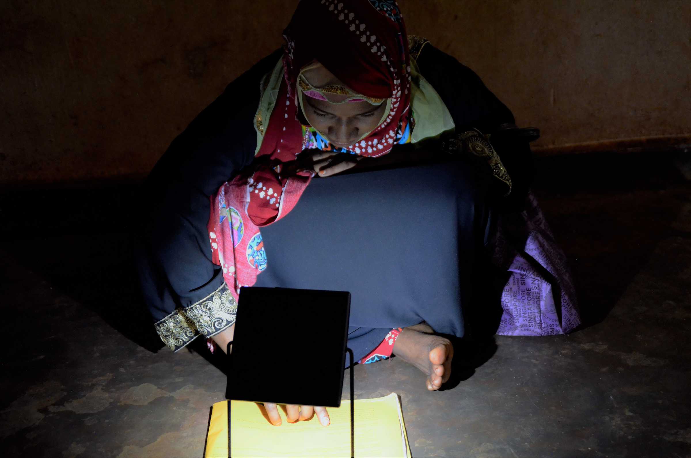 Frau macht Hausübung mit Hilfe einer Solarlampe.