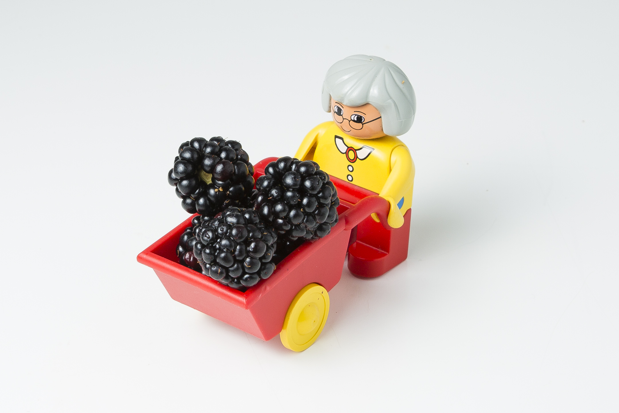 Oma-Legofigur die eine Scheibtruhe mit Brombeeren hält